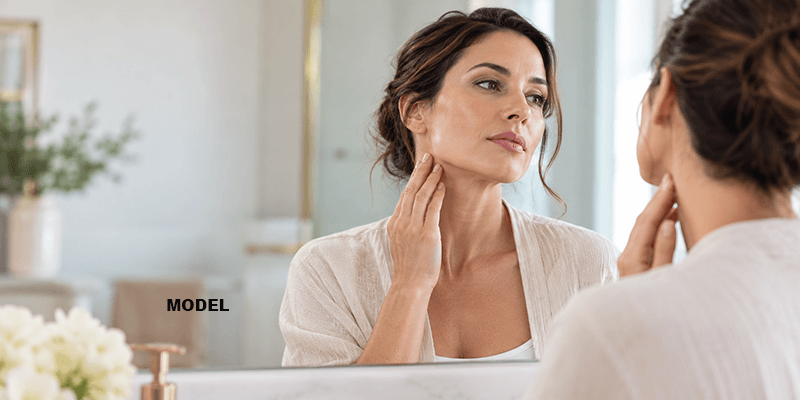 younger woman in her 30s examining neck and jaw in mirror